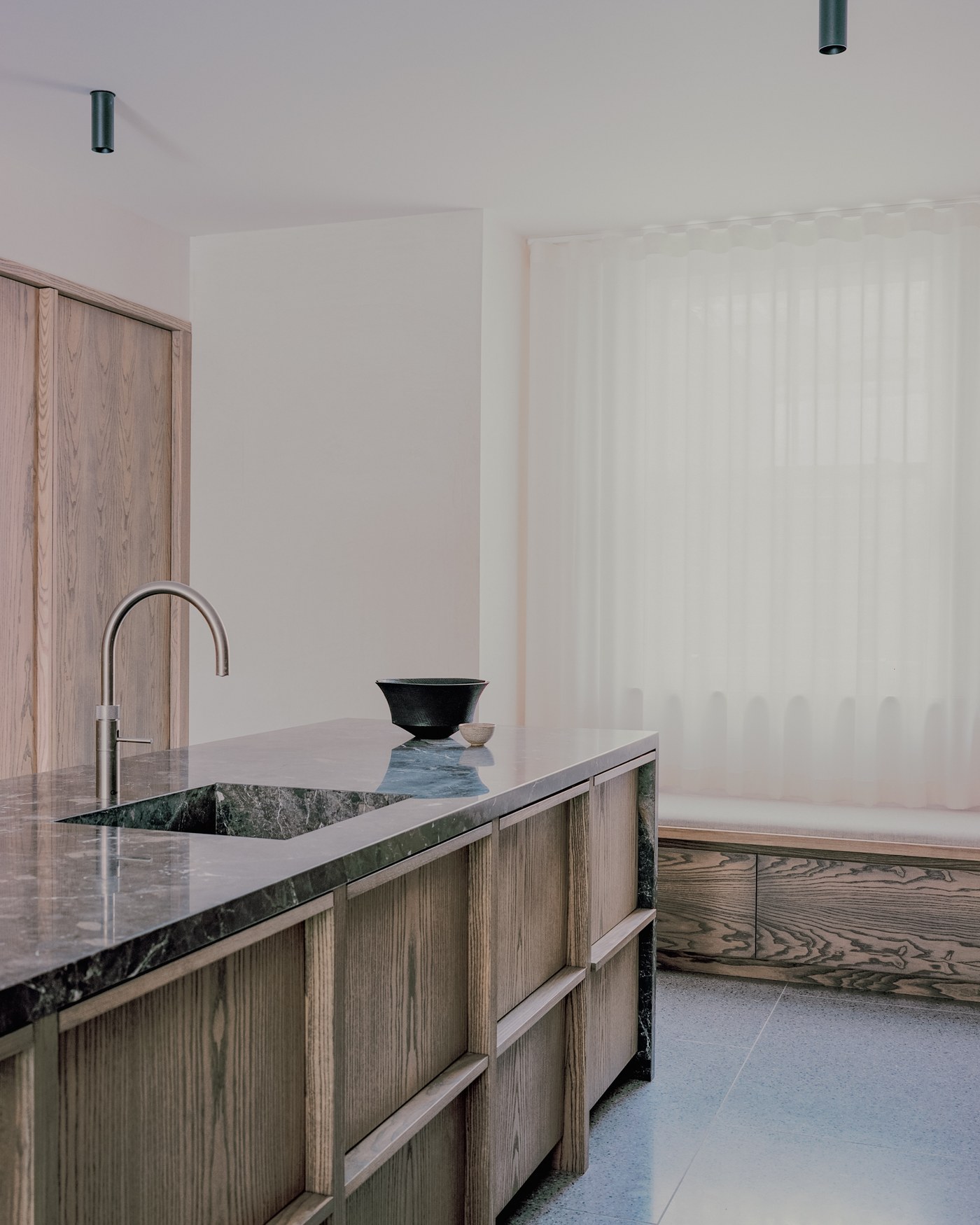 Caithness Road W14 — close view of the stone-topped kitchen island with its framed ash panels and an ash window seat beyond