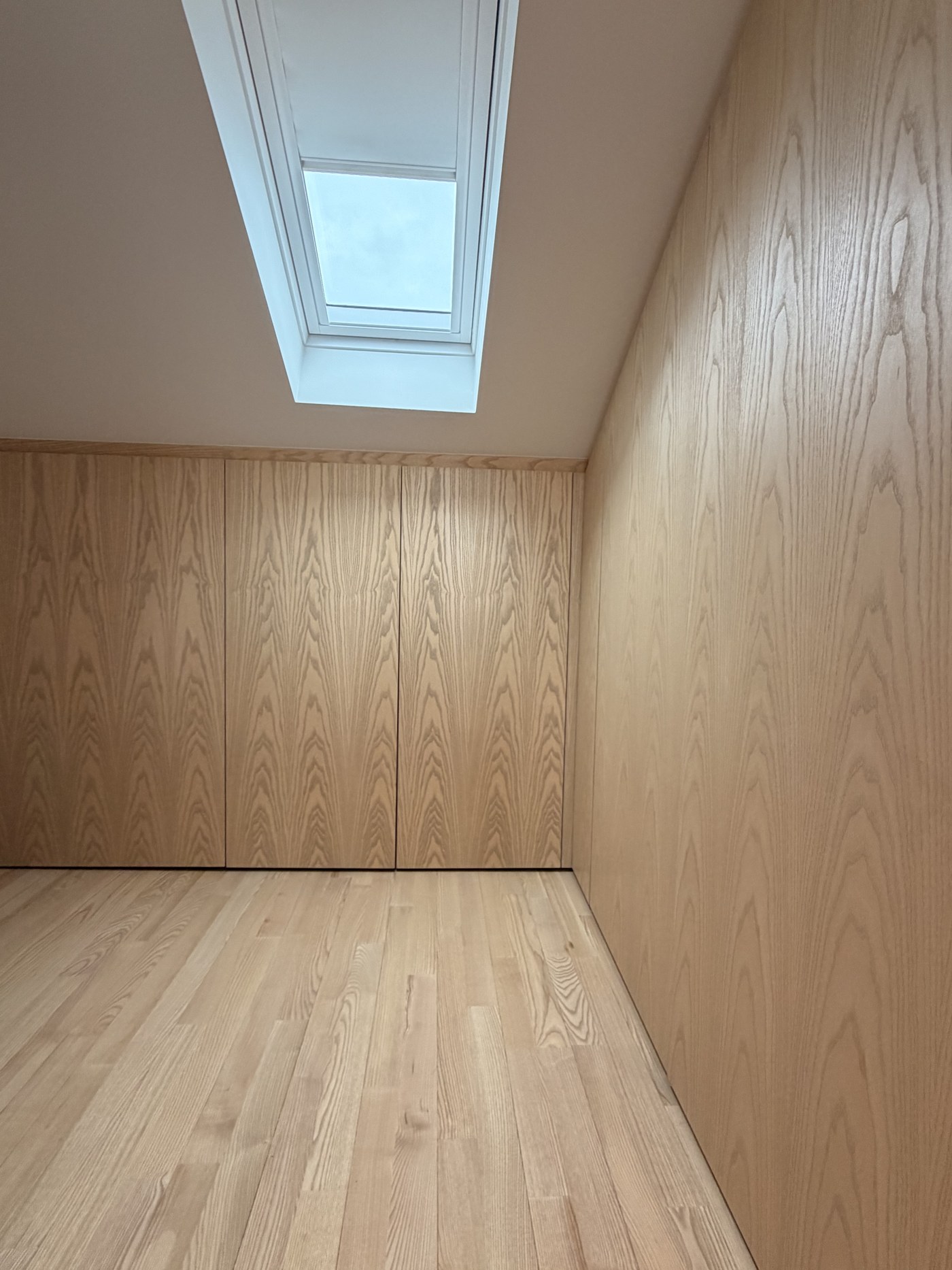 Caithness Road W14 — full-height flush ash wardrobes and ash wall panelling beneath a rooflight, over a timber floor