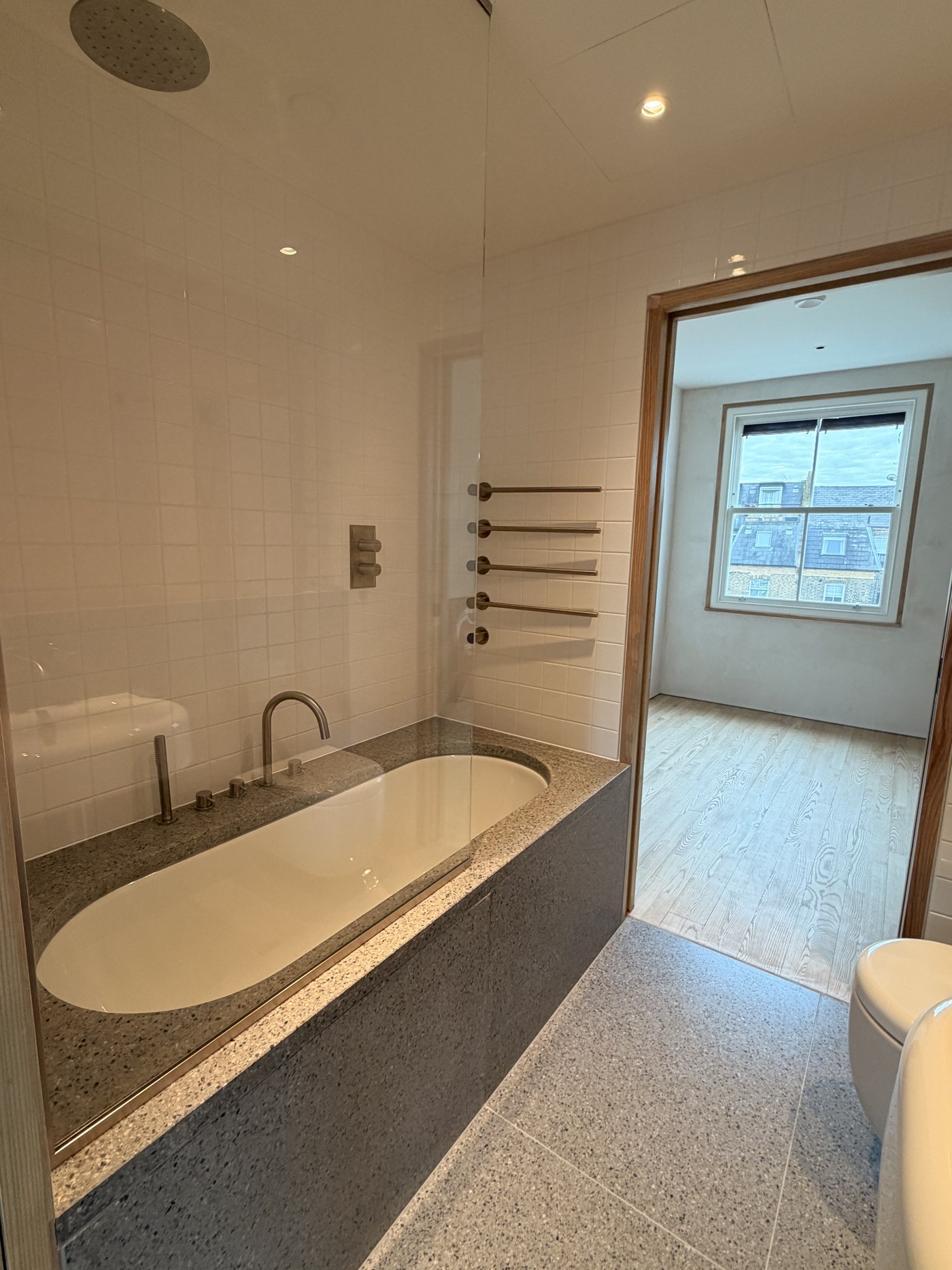 Caithness Road W14 — bathroom with a stone-clad bath, frameless glass screen and white tiling, opening to a bedroom with a sash window