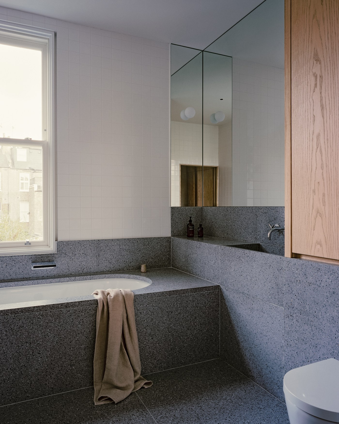 Caithness Road W14 — bathroom with the bath, floor and walls in speckled stone, with ash joinery and mirrored cabinet
